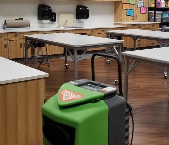 Class room with tables no chairs and one lone green dehumidifier